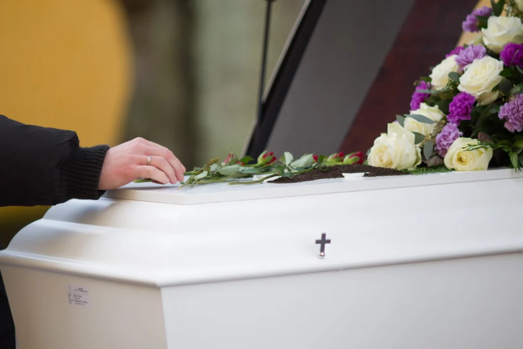 Close-up shot of a person's hand resting on a casket with a blurred background.