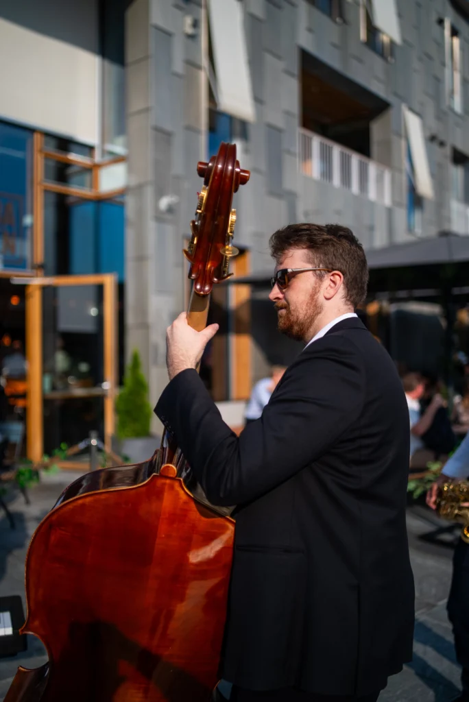 A jazz double bass player performing outdoors in a suit, with a city setting in the background.