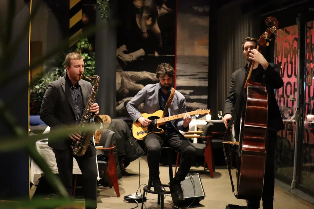 Live music and event services in a cozy restaurant, featuring a saxophonist, guitarist, and double bassist, with warm lighting and an intimate atmosphere.