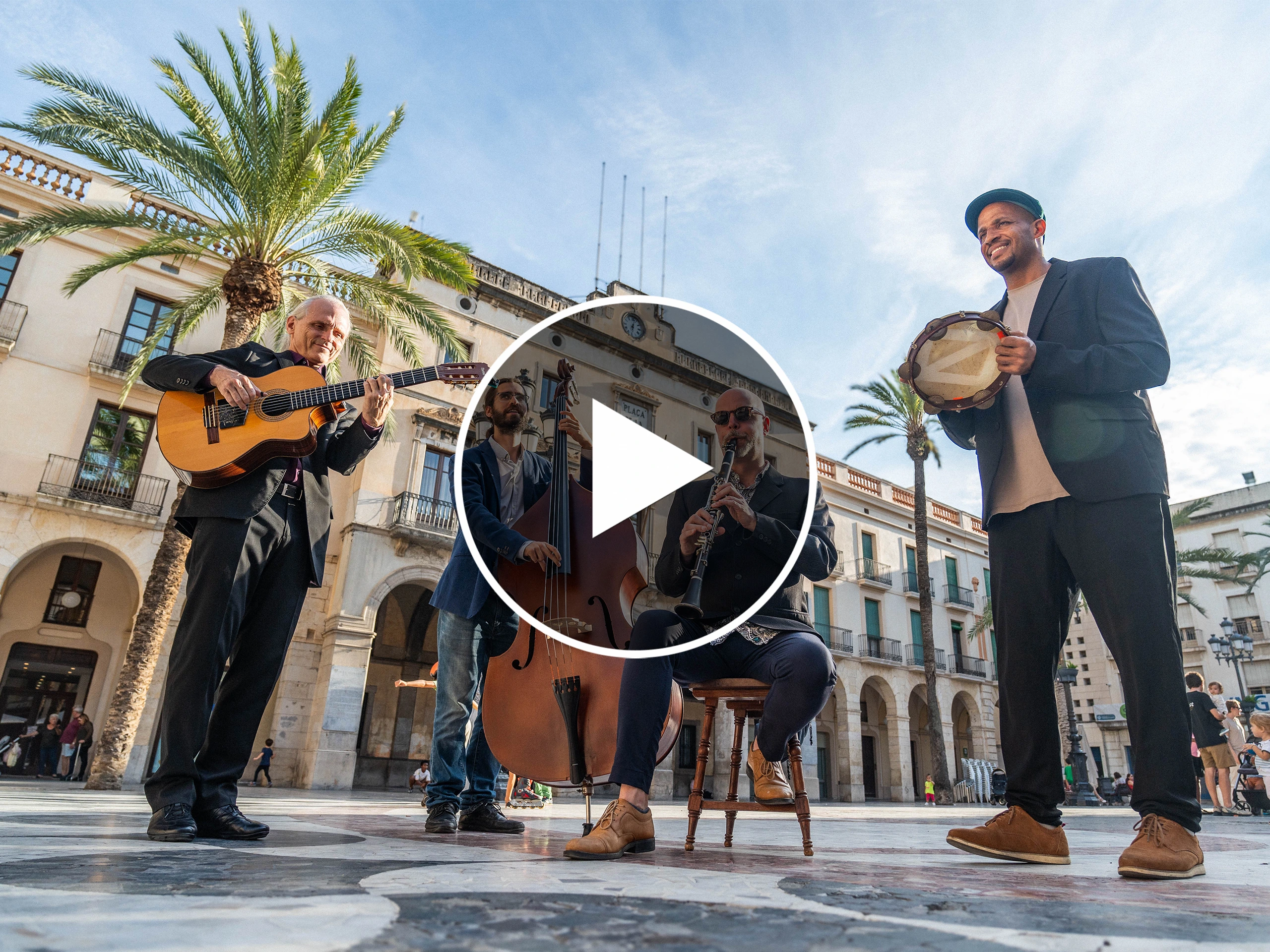 Street musicians performing outdoors in Norway, featuring a guitarist, double bassist, clarinetist, and tambourine player under palm trees in a public square.